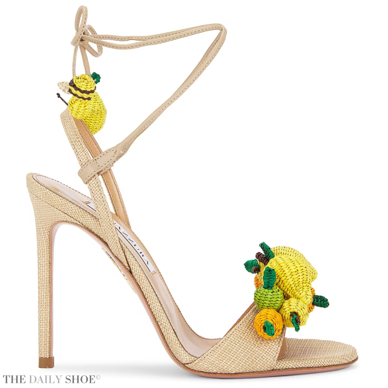 A pair of Aquazzura Citrus Punch 105 raffia sandals in a vibrant shade of yellow, featuring orange and lime green accents and playful lemon and honeybee embellishments.